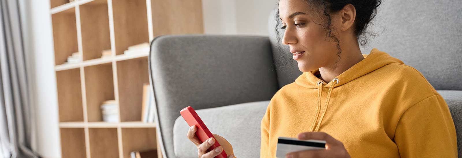 Junge Frau im gelben Pullover hält ein iPhone und eine Kreditkarte in der Hand